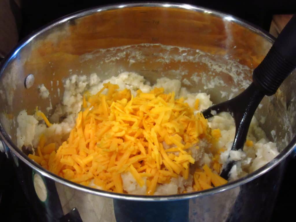 Shredded cheddar cheese in a pot of mashed potatoes.