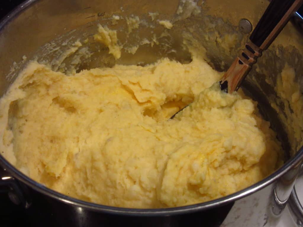 A large pot filled with cheesy horseradish mashed potatoes and a wooden spoon.