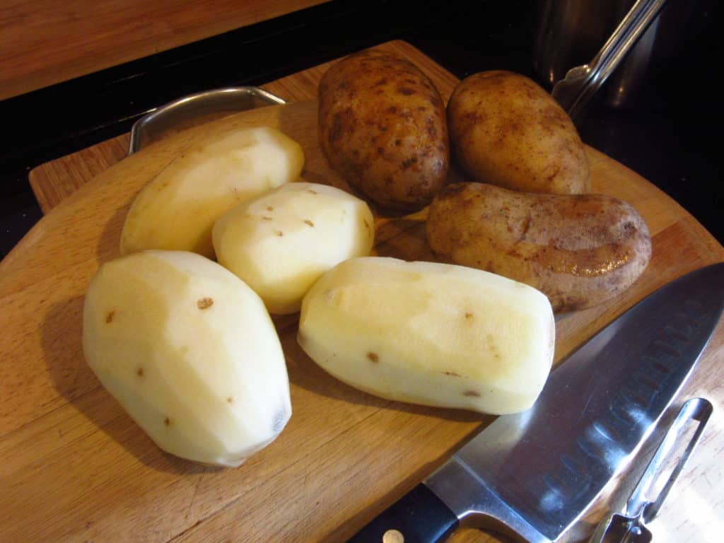 Potatoes, peeled and unpeeled on a cutting board.