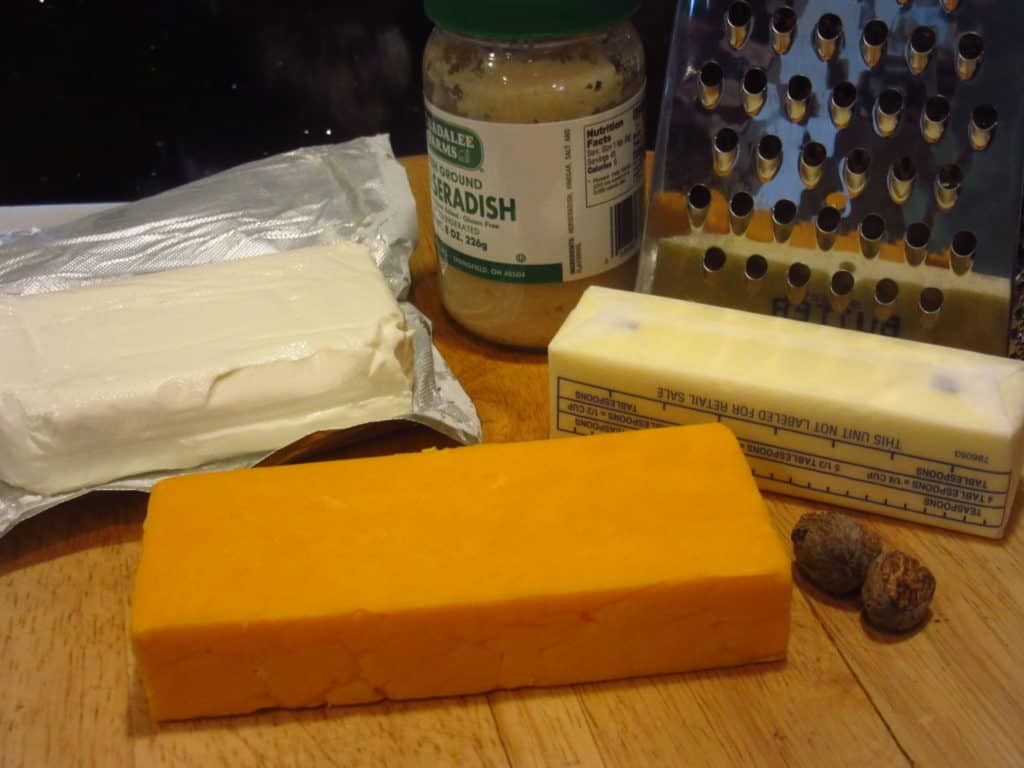 Cheese and butter on a cutting board with a box grater in the background.