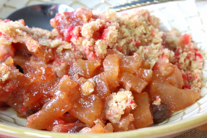 Closeup horizontal photo of a bowl of apple crisp with raisins and crushed cinnamon candy topping.