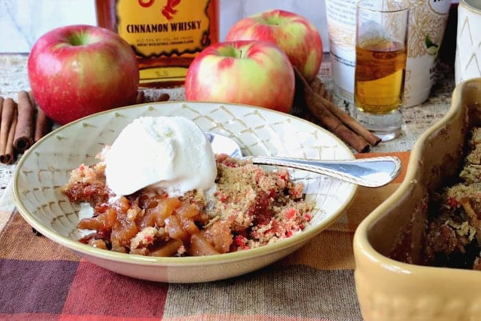 A bowl of fireball apple crisp with a scoop of vanilla ice cream and a spoon.