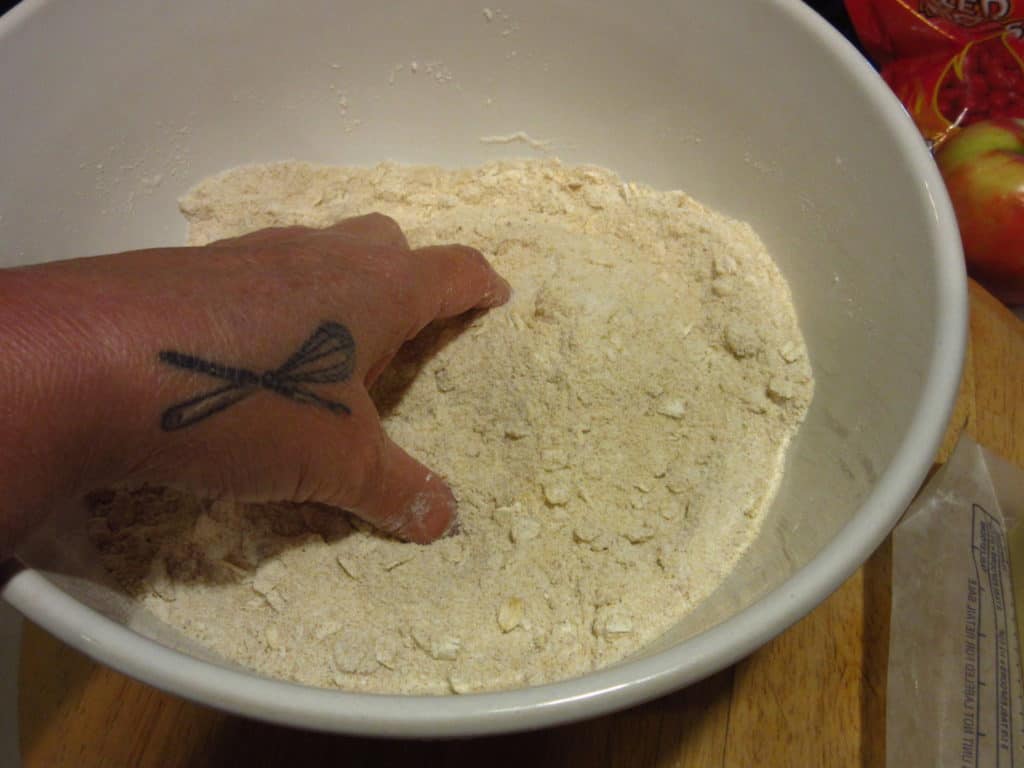 A hand mixing ingredients in a large white bowl.