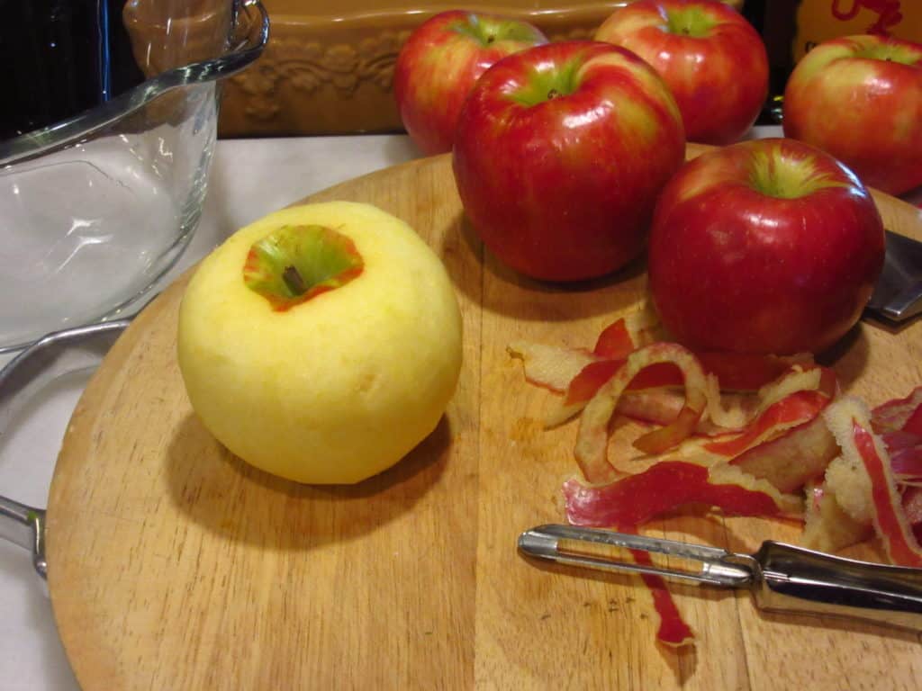Apples on a cutting board with an apple peeler.