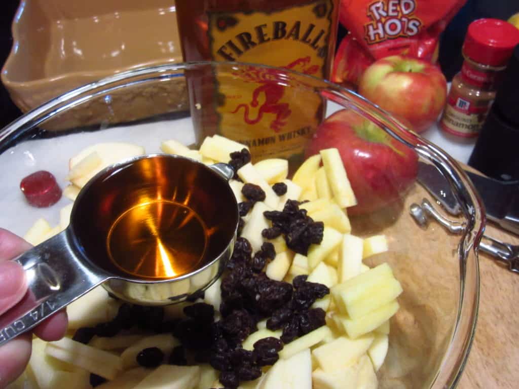 Fireball whiskey being added to diced apples in a bowl.