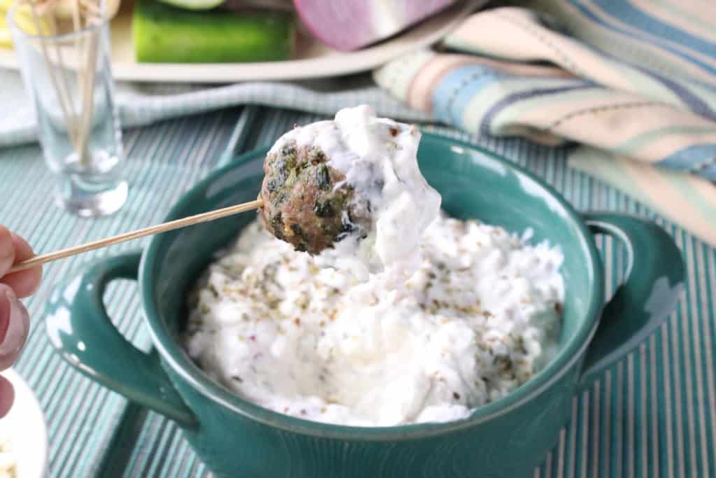 A Greek meatball appetizer on a toothpick with tzatziki sauce.