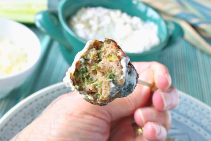 A closeup of a Greek meatball appetizer with spinach and feta cheese with a bite taken out.