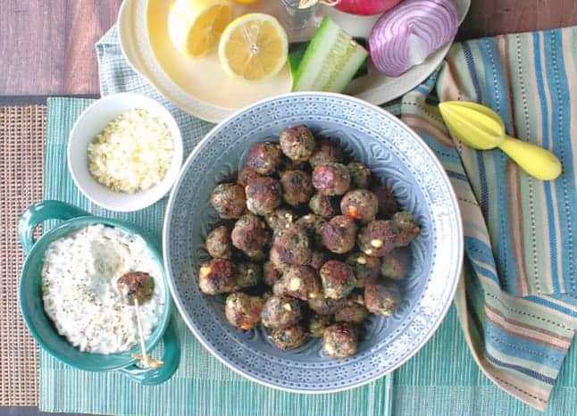 Overhead photo of a bowl of Greek appetizer meatballs with feta cheese and tzatziki sauce, cucumber, onion, and lemon.