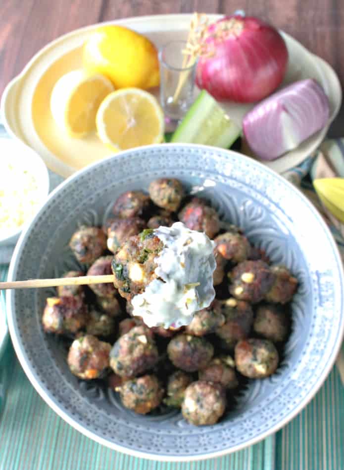 A closeup of a Greek meatball appetizer on a toothpick that has been dunked in tzatziki sauce.
