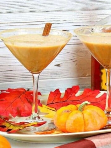 Two martini glasses filled with pumpkin spice martinis and autumn leaves on a platter