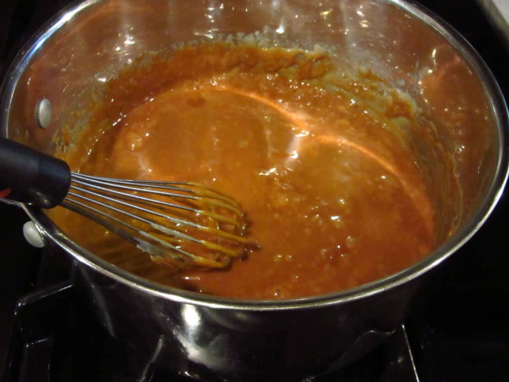A brown toffee in a saucepan with a whisk.