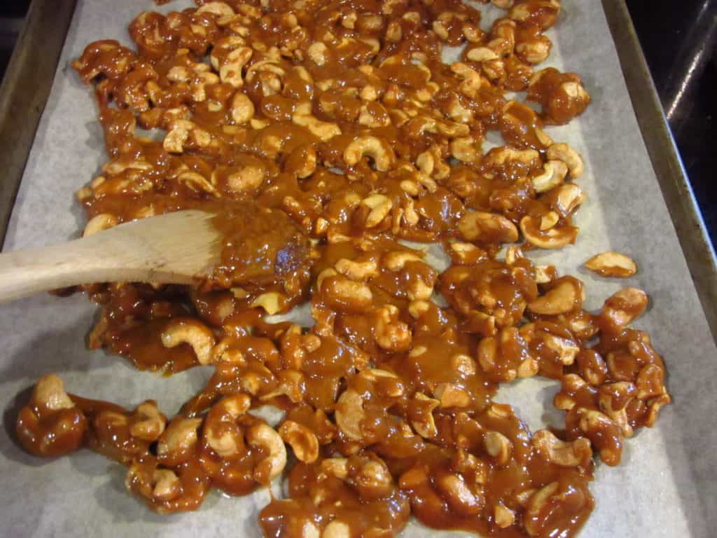Cashew toffee spread out on a parchment baking sheet.