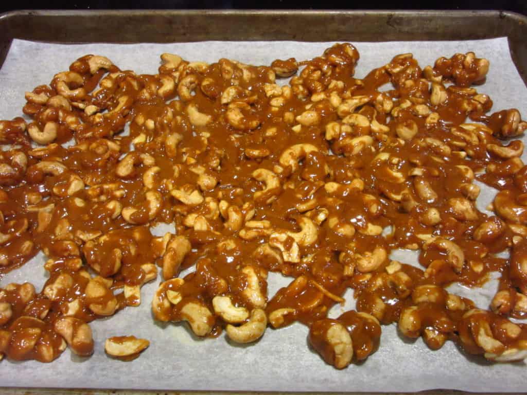 Cashew toffee spread out on a parchment baking sheet.