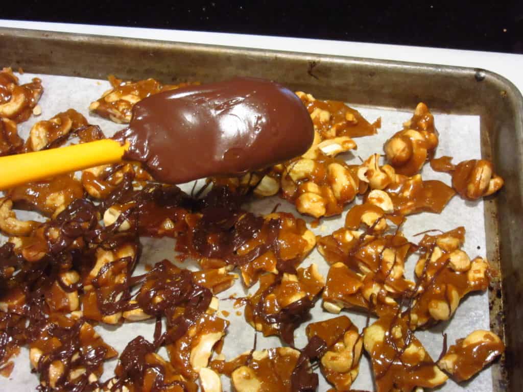 Melted chocolate being drizzled over cashew toffee.