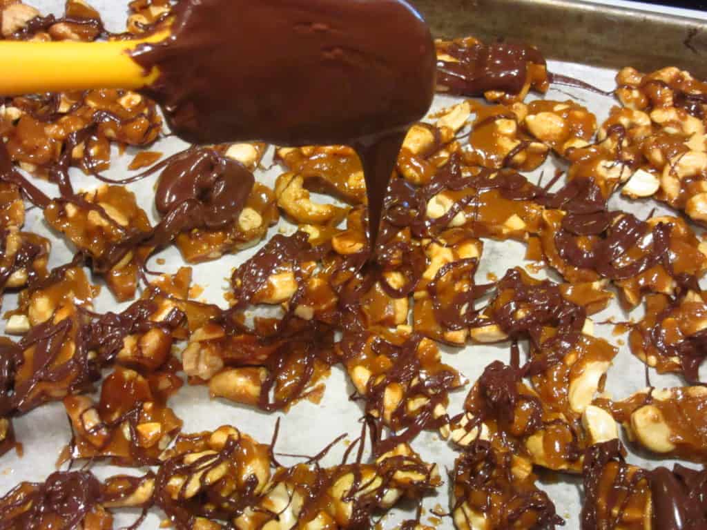 Melted chocolate being drizzled over cashew toffee.