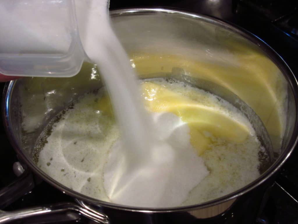 Sugar being added to melted butter in a saucepan.