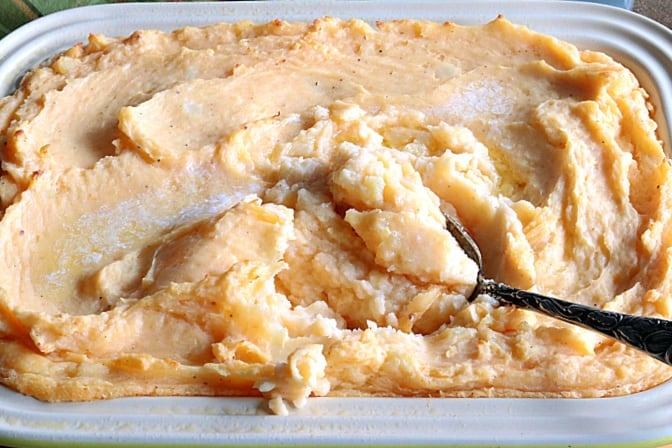 Closeup vertical photo of a casserole dish filled with make-ahead cheesy horseradish mashed potato casserole with a serving spoon.