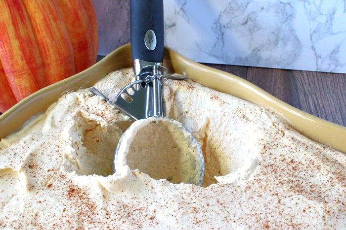 An ice cream scoop tucked inside a creamy container of no churn pumpkin ice cream.