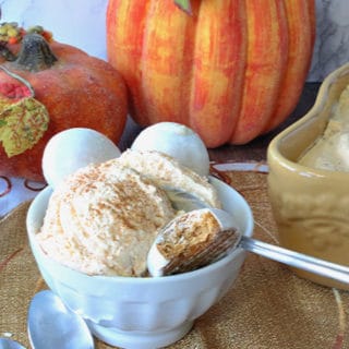 A small white bowl with a scoop of pumpkin pie ice cream, a spoon, and cookies.