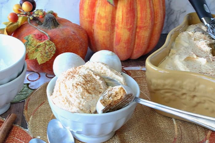 A small white bowl with a scoop of pumpkin pie ice cream, a spoon, and cookies.