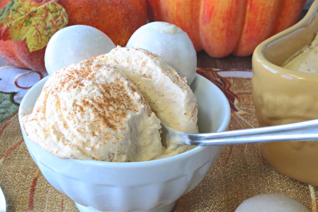 A creamy dish of no churn pumpkin ice cream with cinnamon sprinkled on top and a spoon.