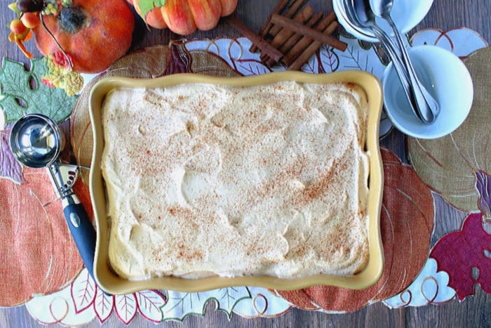 Overhead picture of a oblong dish filled with pumpkin ice cream, sprinkled with cinnamon, and an ice cream scoop on the side.