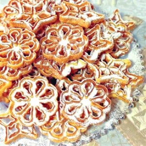 A stack of Fried Rosette Snowflake Cookies with icing sugar on top.