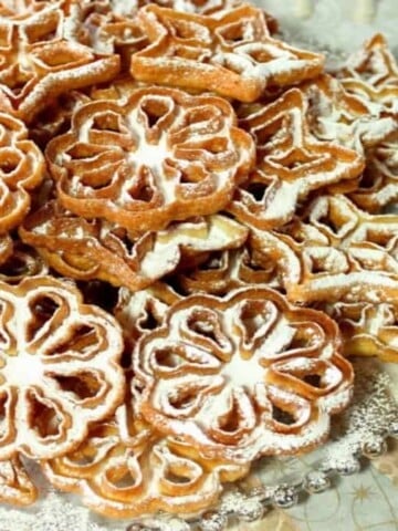 A round glass platter filled with rosette snowflake cookies with confectioners sugar dusting