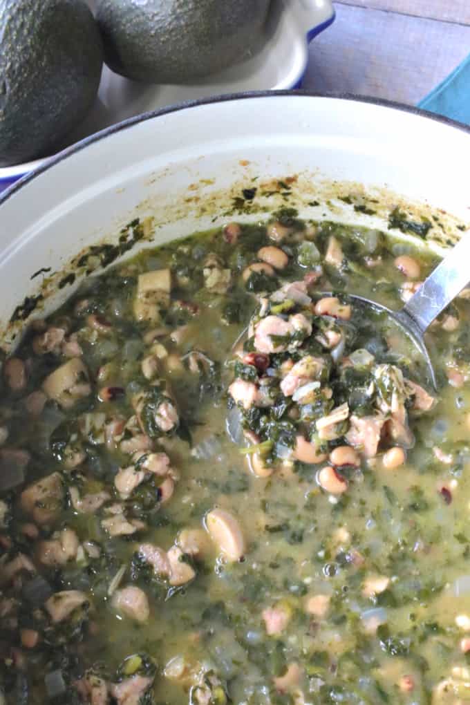 A closeup vertical photo of a pot of black-eyed pea chicken chili with a ladle.