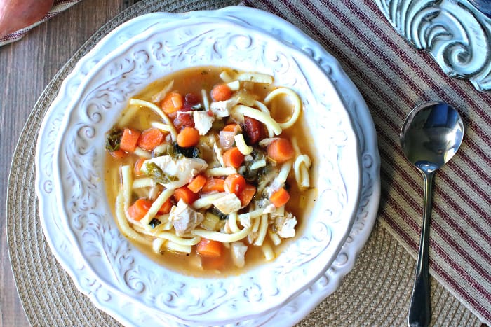 Overhead horizontal photo of a hearty and delicious bowl of chicken and leek soup with a striped napkin and a soup spoon on the side.