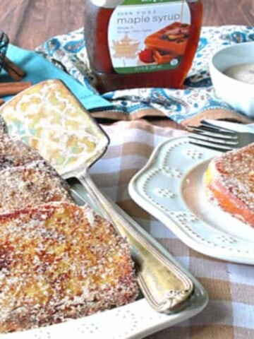 A table set up with breakfast of cinnamon sugar french toast with eggs and syrup in the background