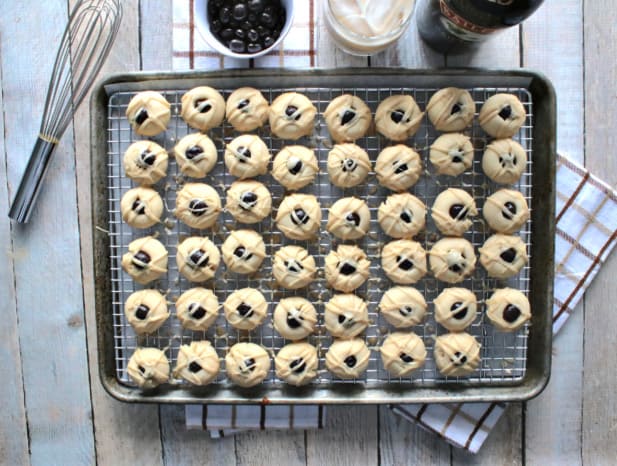 Overhead horizontal photo of a baking sheet filled with Irish cream butter cookies, a whisk, chocolate covered espresso beans and a glass or Irish cream liquor.
