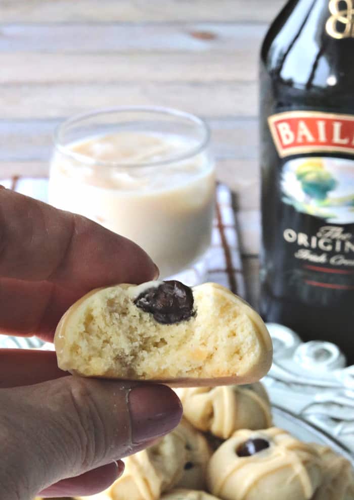 A vertical closeup photo of an Irish cream butter cookie with a bite taken out of it and a bottle of Irish cream and a glass in the background.