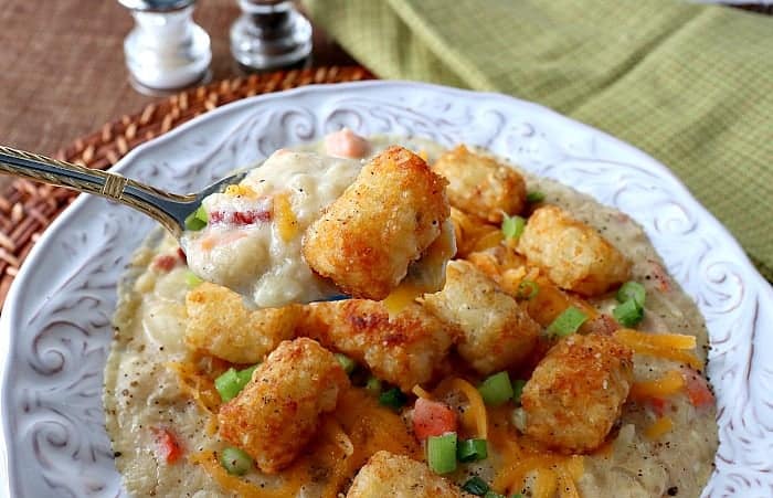 A horizontal photo of a closeup soup spoon filled with tater tot chowder and a tater tot with cheese and green onions. Comfort food soups, stews, and chowders recipe roundup.