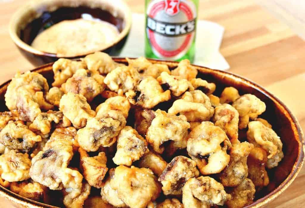 Beer battered fried mushrooms in a brown oval bowl with a bottle of beer in the background