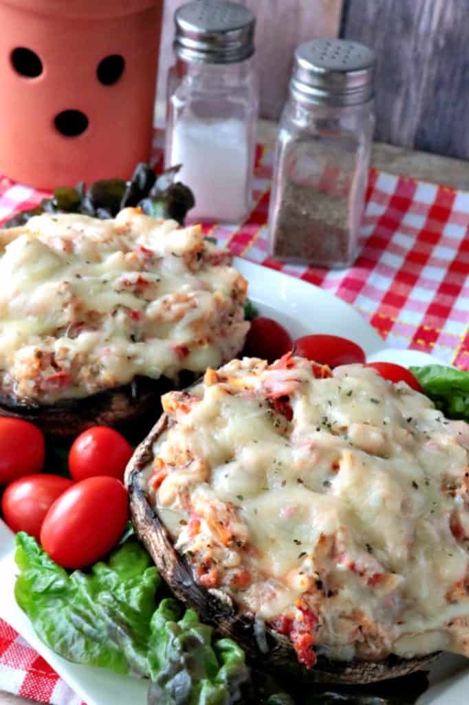 A vertical closeup photo of two chicken Parmesan stuffed portobello mushrooms on a plate with lettuce and grape tomatoes.