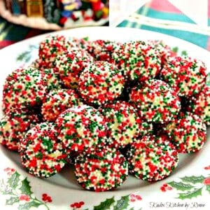 A holly berry plate stacked high with Christmas Cream Cheese Sprinkle Cookies.