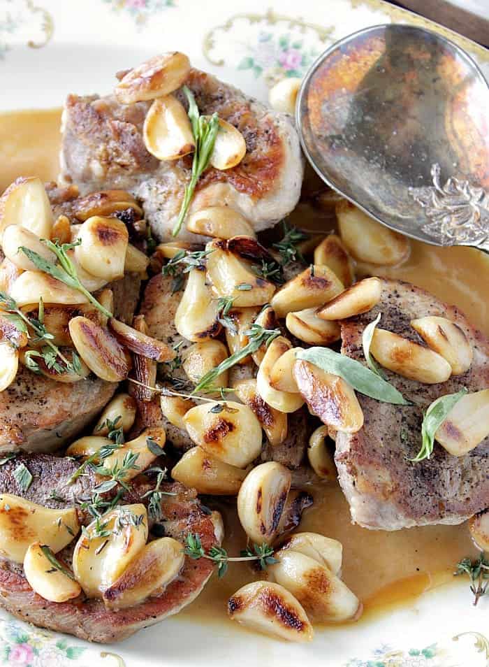 A beautiful vertical closeup photo of garlic lovers pork chops with browned garlic, fresh herbs and a serving spoon.