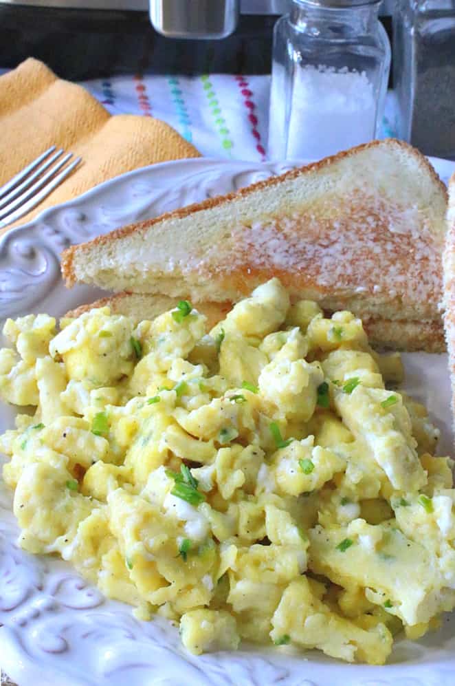 Closeup vertical image of air fryer scrambled eggs on a white plate with buttered toast in the background.