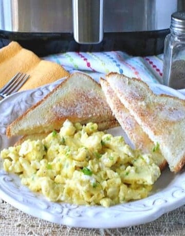 A plate of air fryer scrambled eggs with toast and a salt and pepper shaker in the background.