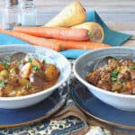 Two bowls of beef stew with carrots and parsnips in the background