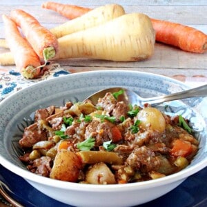 A blue bowl filled with a serving of Beef Stew for a Crowd with carrots and parsnips.