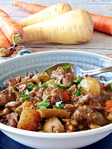 A blue bowl filled with a serving of Beef Stew for a Crowd with carrots and parsnips.