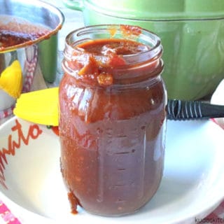 A jar of salsa BBQ sauce in a bowl with a brush and a saucepan in the background.