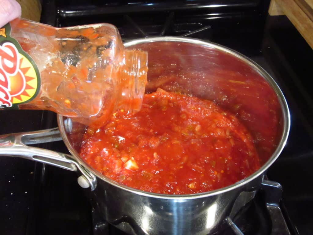 A jar of salsa being poured into a saucepan.