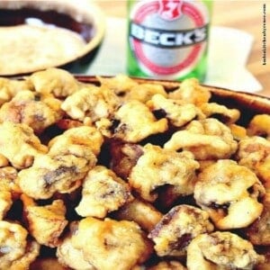 A pile of Beer Battered Deep Fried Mushrooms in a bowl with a beer in the background.