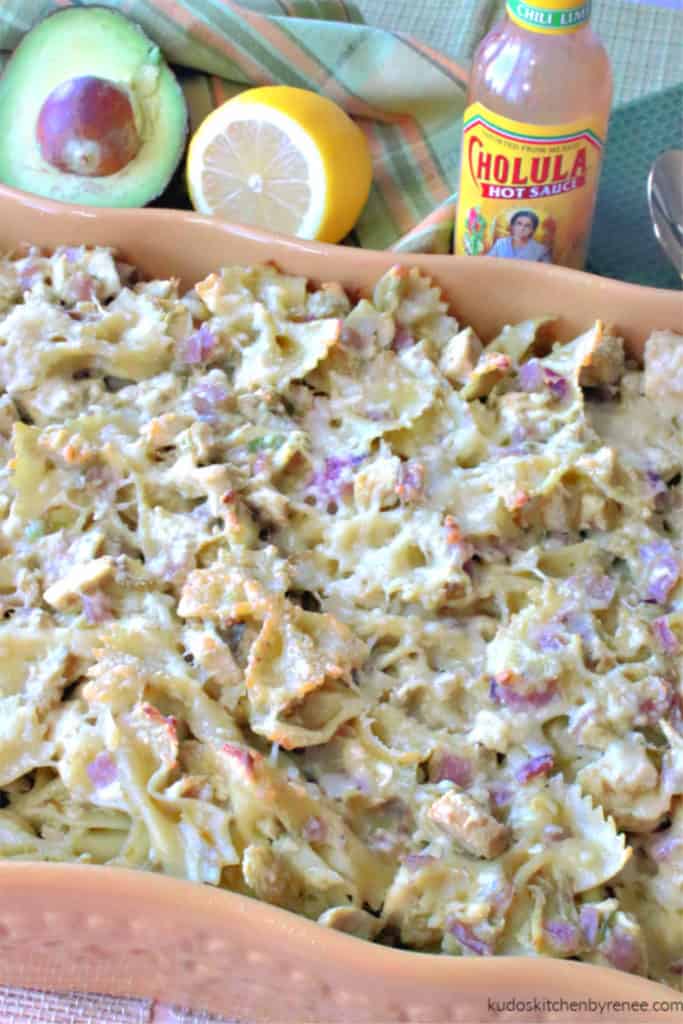 A vertical closeup photo of a casserole dish filled with chicken and pasta with artichokes and avocados.