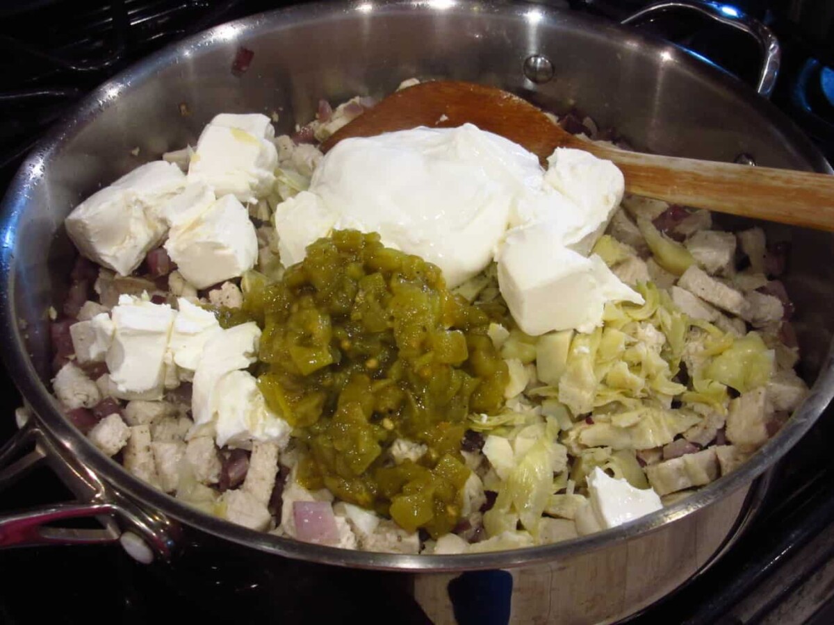 Cream cheese and fire roasted chiles being added to a pot on the stovetop.