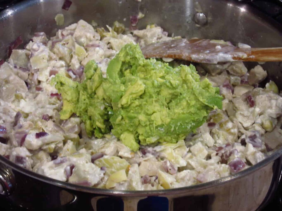 Mashed avocado in a bowl of chicken with artichoke.