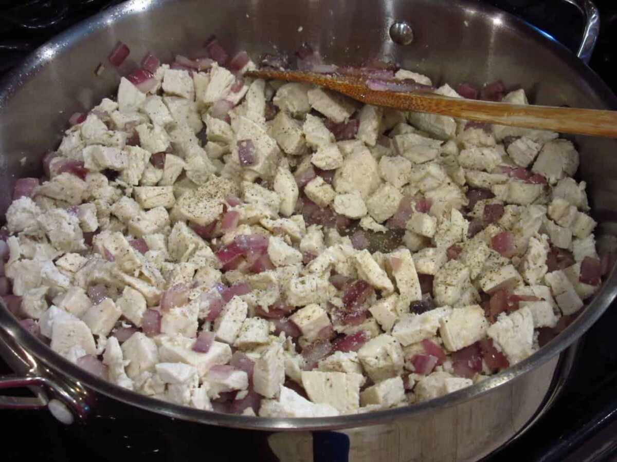 Cooked chicken and red onion in a pan on the stovetop.
